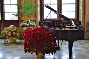 brown grand piano beside red flowers