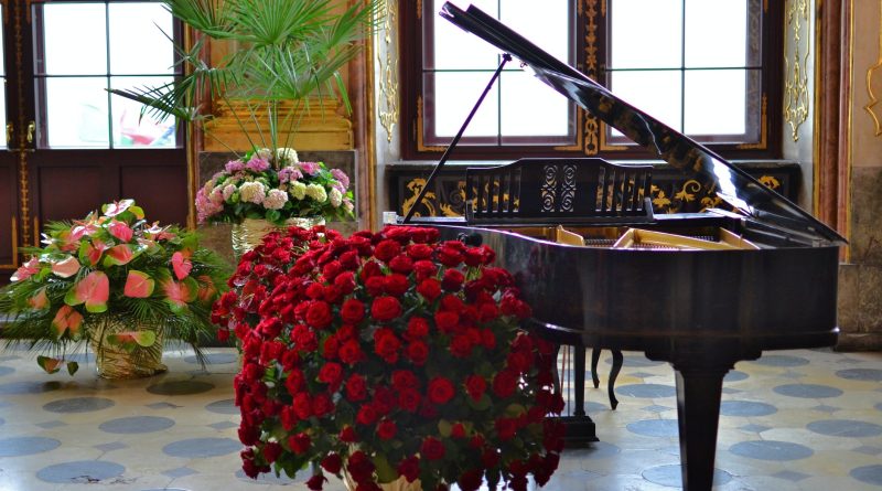 brown grand piano beside red flowers